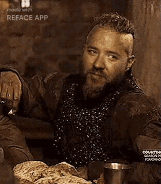 a man with a beard is sitting at a table with bread and a cup of beer .