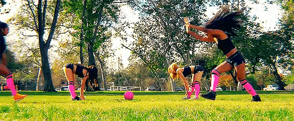 a group of women are playing soccer in a park with trees in the background