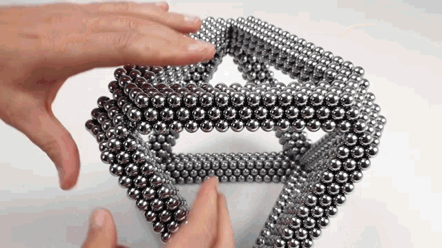 a person is playing with a stack of metal balls on a white surface