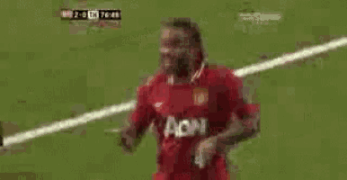 a soccer player wearing a red aon jersey stands on the field