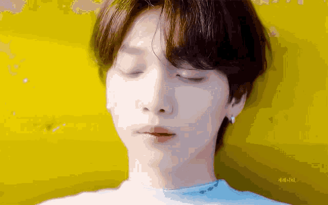 a close up of a young man with his eyes closed against a yellow wall .