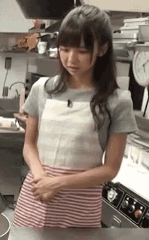 a girl wearing an apron is standing in a kitchen .