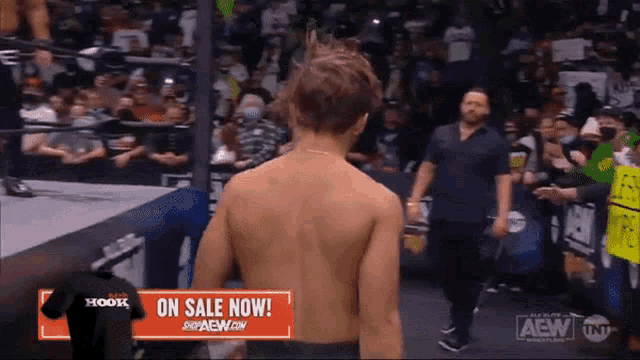 a man without a shirt is standing in front of a crowd with a sign that says on sale now .
