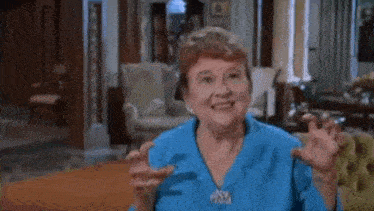 a woman in a blue shirt is sitting on a couch in a living room smiling .