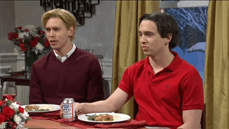 two men in red polo shirts sit at a table with plates of food