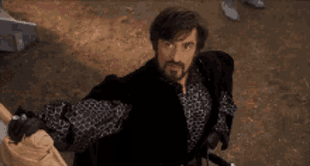 a man with a beard and mustache is holding a sword and a hat .