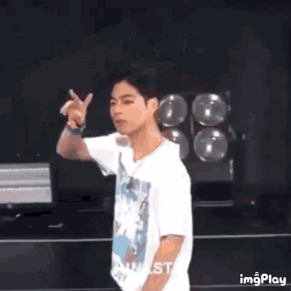 a young man in a white shirt is giving a peace sign while standing on a stage .