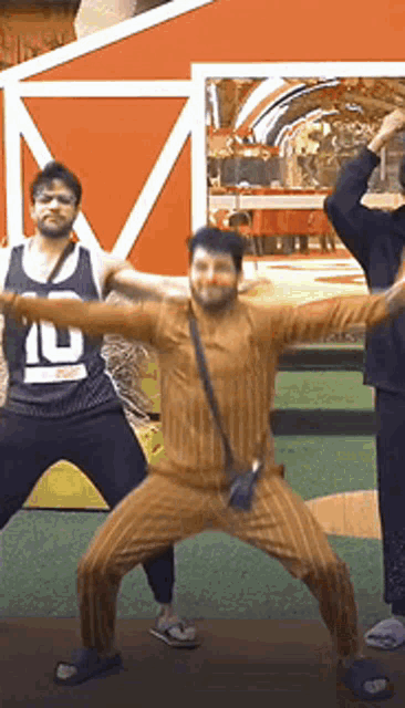 a group of men are dancing in front of a red barn . one of the men has the number 10 on his shirt .