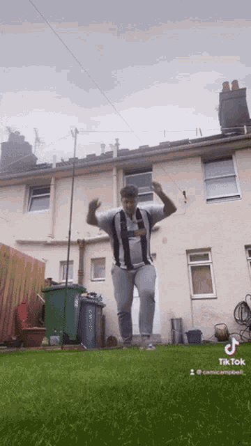 a man is dancing in front of a house with a green trash can in the background