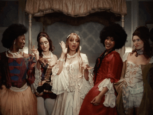 a group of women dressed in historical costumes are standing in a room