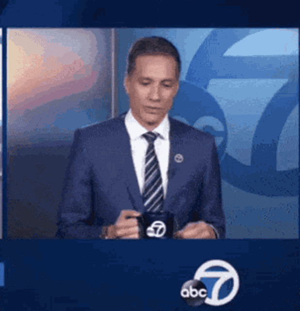 a man in a suit and tie is holding a mug with abc on it