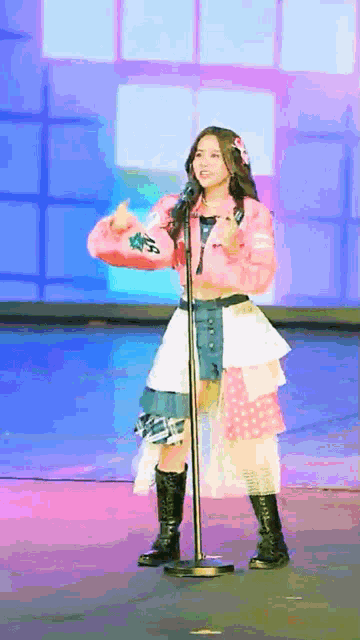 a girl in a pink jacket is singing into a microphone while wearing black boots