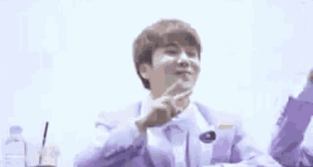 a man in a purple suit and bow tie is making a peace sign with his finger .