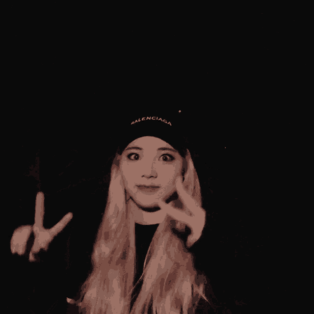 a blonde woman wearing a black hat making a peace sign with her hands