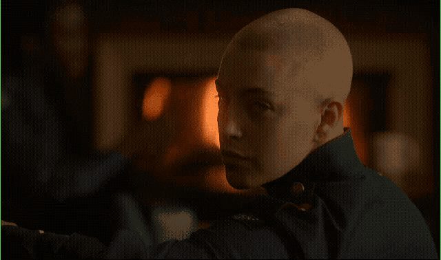 a man with a shaved head is standing in front of a fire