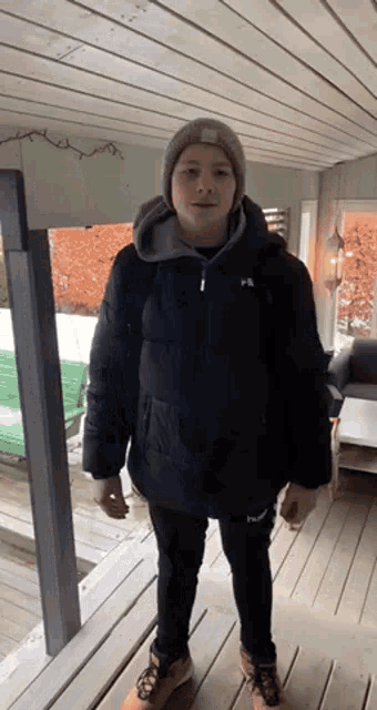a young man wearing a black jacket and a grey beanie is standing on a porch .