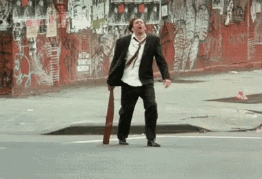 a man in a suit and tie is walking down the street holding a baseball bat
