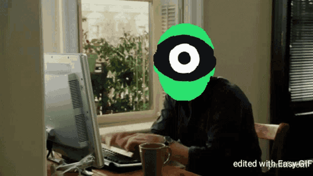 a man is sitting at a desk with a computer and a green face with an eye on it