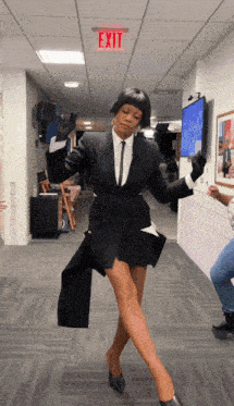 a woman in a suit is dancing in a hallway with an exit sign above her