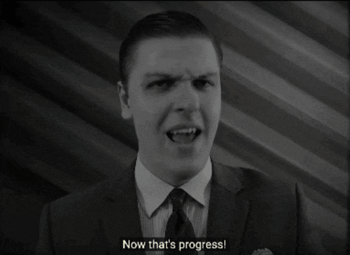 a man in a suit and tie says " now that 's progress " in a black and white photo