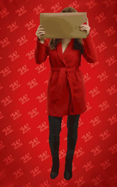 a woman in a red coat is holding a cardboard box in front of a wall that says 547 miljoen