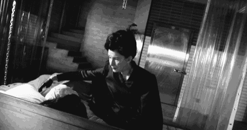 a black and white photo of a man standing next to a coffin with a woman laying in it .