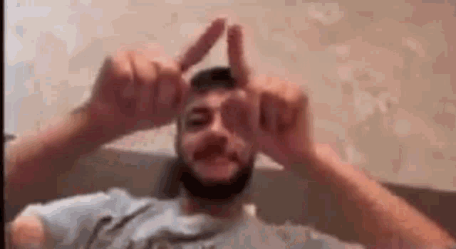 a man with a beard is making a peace sign with his hands while sitting on a bed .