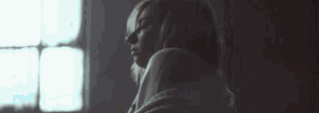 a woman is standing in front of a window and looking down