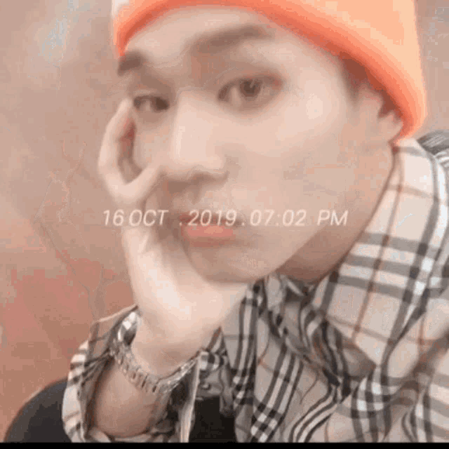 a man wearing a plaid shirt and an orange beanie is sitting with his hand on his chin .
