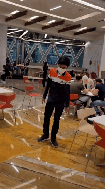 a young man wearing a mask stands in a restaurant