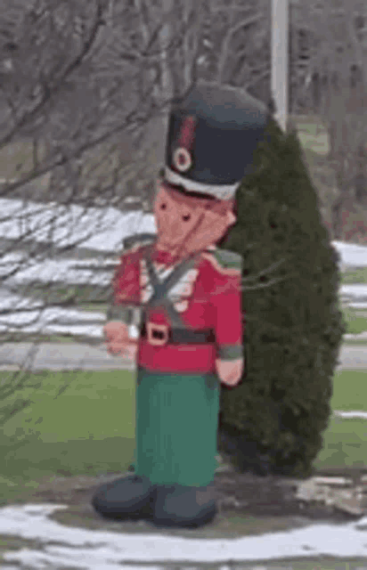 a large inflatable nutcracker is standing next to a tree in a park .