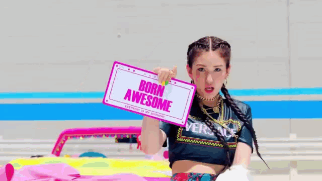 a woman in a versace shirt is holding a sign that says born awesome