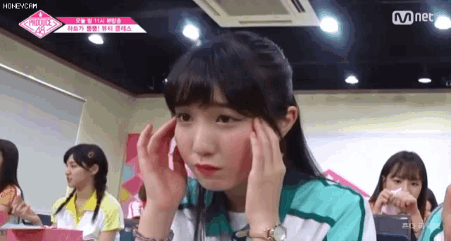 a girl is holding her head in pain while sitting in a classroom .