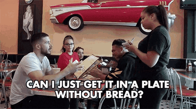 a group of people are sitting at a table in a diner talking to a waitress who is taking orders .