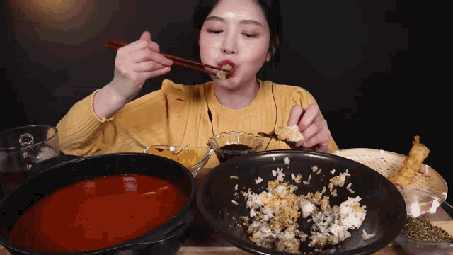 a woman in a yellow sweater is eating food with chopsticks and a bowl of rice
