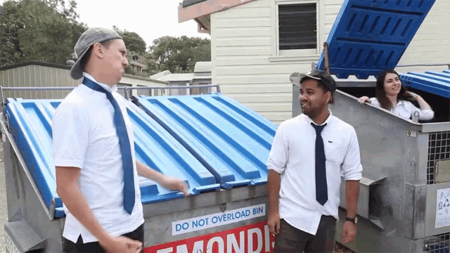 a man standing next to a dumpster that says " do not overload bin "