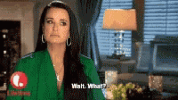 a woman in a green shirt is standing in front of a window and talking to someone .