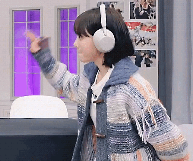 a woman wearing a sweater and headphones is waving her hand