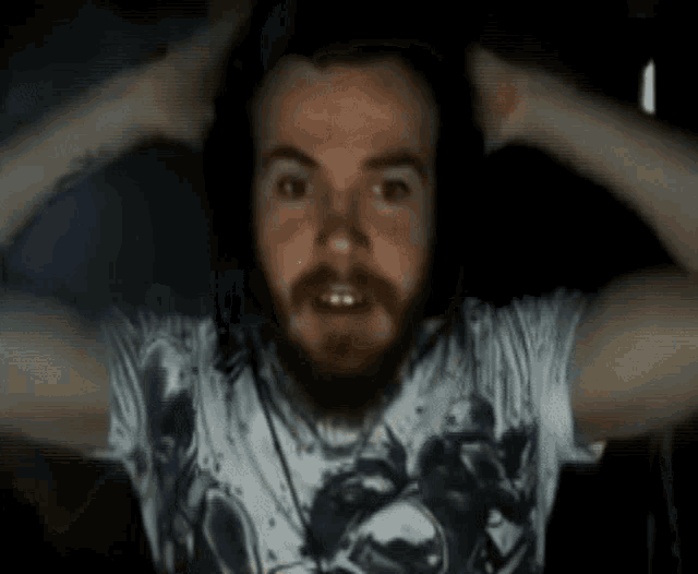 a man with a beard wearing headphones and a t-shirt is holding his head .