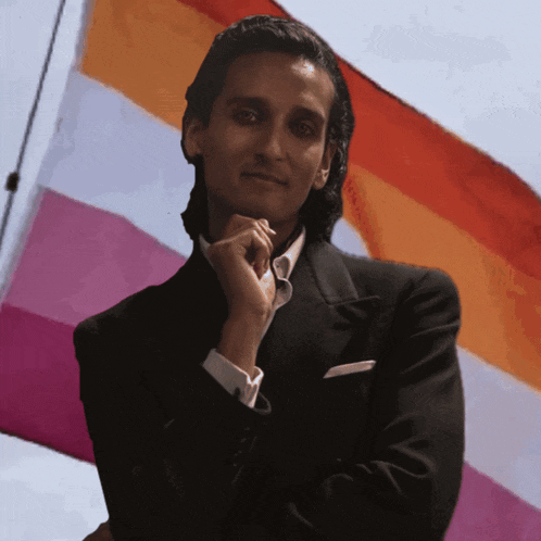 a man in a tuxedo stands in front of a flag