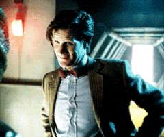 a man in a suit and bow tie stands in a dark room with his hands on his hips
