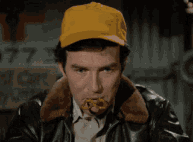 a man wearing a yellow hat and a leather jacket eating something