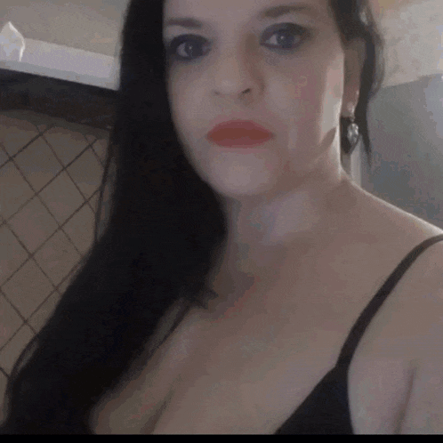 a woman with long black hair and red lipstick is wearing a black bra