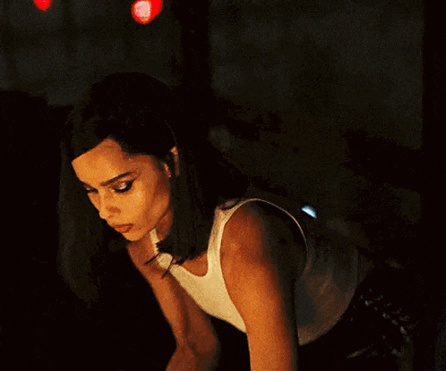 a woman in a white tank top is kneeling down in the dark