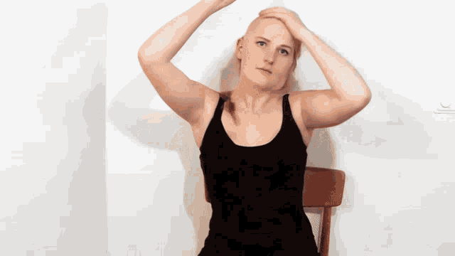 a bald woman in a black tank top is sitting in a chair