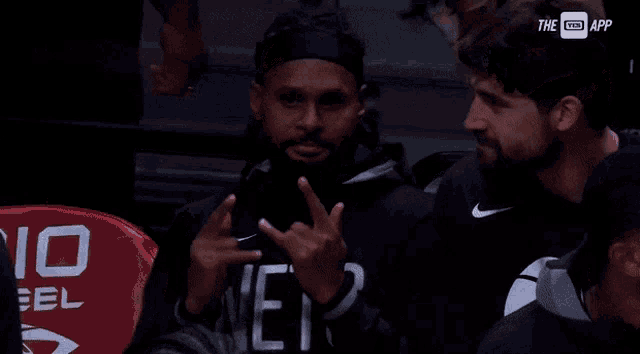 a man wearing a nets sweatshirt sits in the stands at a basketball game