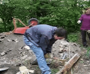 a man in a blue jacket is digging in the dirt while a woman in a purple jacket watches