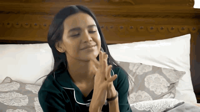 a woman sitting on a bed with her eyes closed and her hands on her face