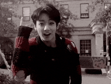 a young man wearing a red and black plaid sweater stands in front of a brick building