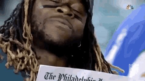 a man with dreadlocks is holding a piece of paper with the philadelphia newspaper on it .